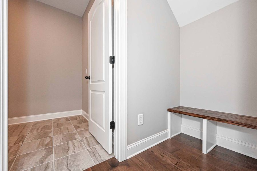 Hallway with a door, bench, and tile and wood flooring.