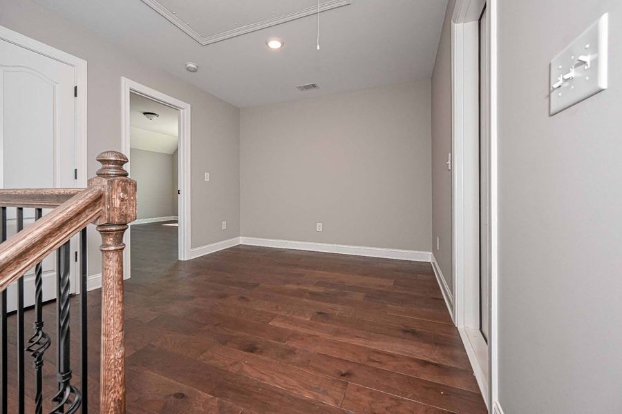 Hallway with hardwood floors, gray walls, and a wooden railing leading to other rooms.
