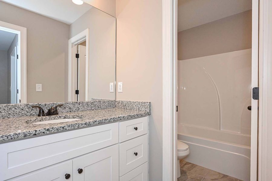 Bathroom with white vanity, granite countertop, large mirror, and tub/shower.
