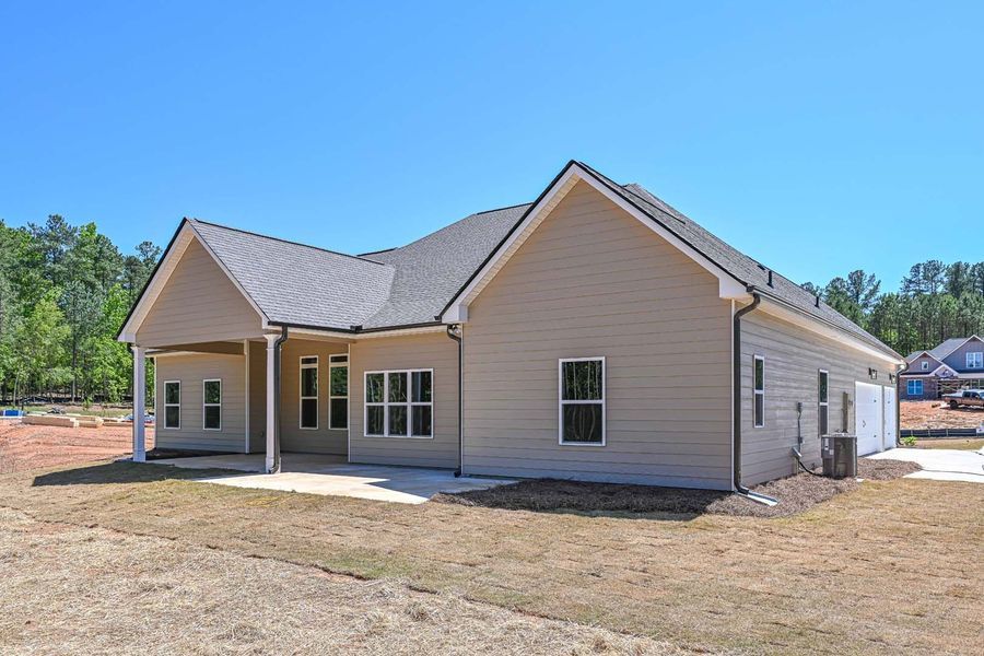 Beige house with a covered patio, gray roof, and blue sky.