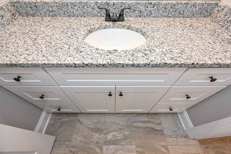 White bathroom vanity with granite countertop and oval sink.
