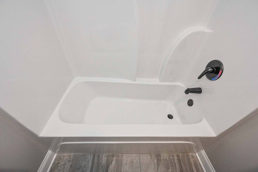 White bathtub in a corner with black faucet and fixtures; light-colored floor.