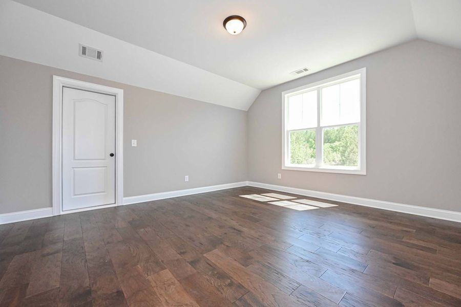 Empty room with hardwood floors, gray walls, white door and window.