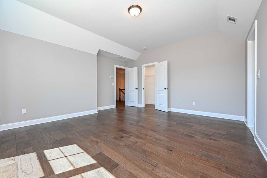 Empty bedroom with gray walls, dark wood floor, white trim, and two doors.