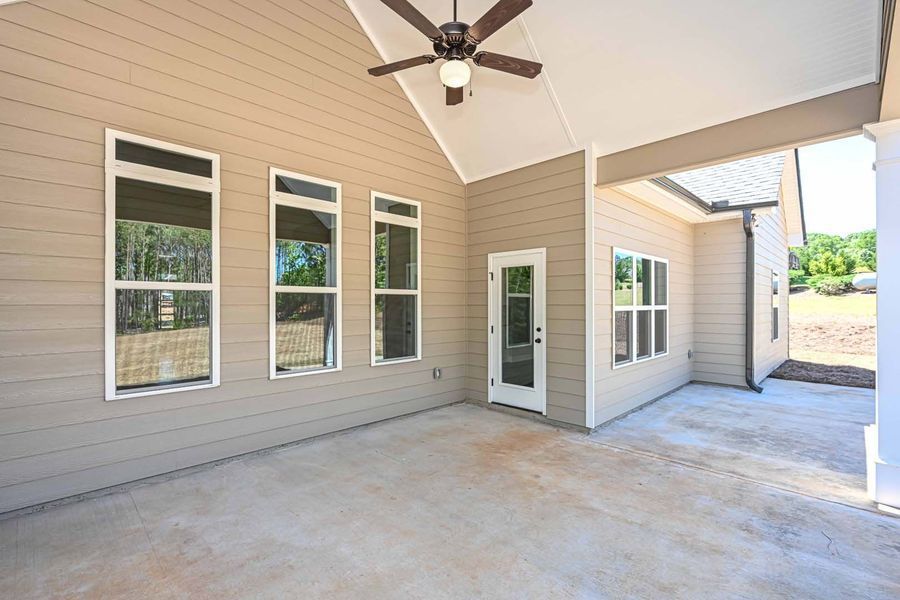 A covered patio with a concrete floor, tan siding, multiple windows, and a ceiling fan.