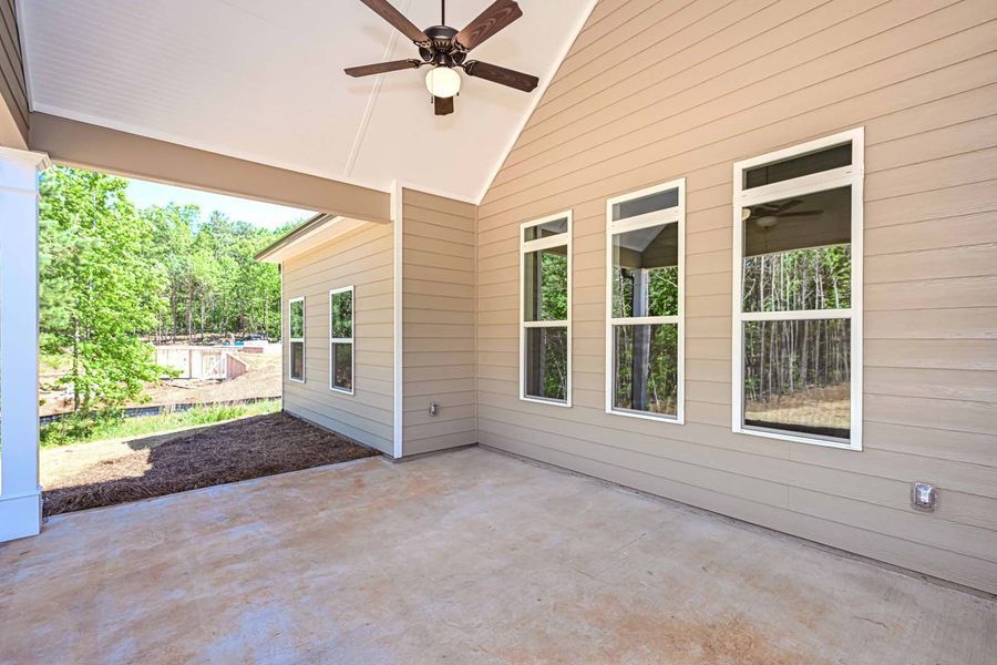 Covered patio with tan siding, concrete floor, windows, and a ceiling fan overlooking a wooded area.