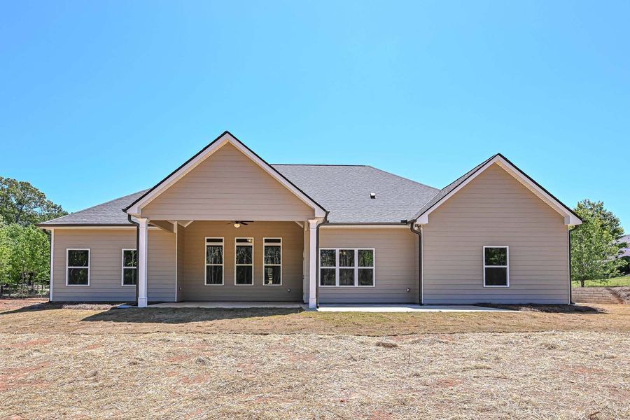 Beige ranch-style house with a covered patio, set against a blue sky and dry grass yard.