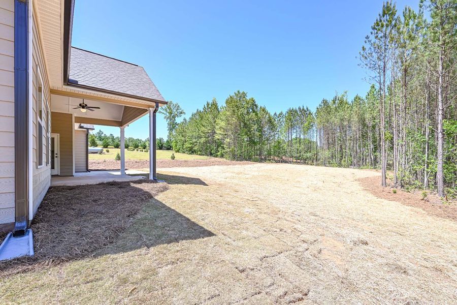 Backyard with covered porch, grassy area, trees in background, clear blue sky.