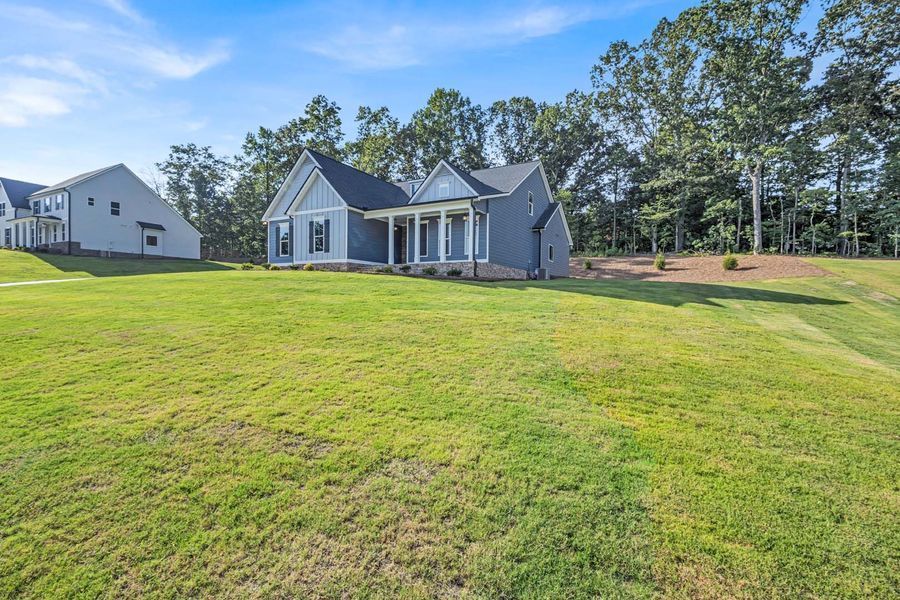 Blue house with white columns on a grassy hill with trees and a partly cloudy sky.