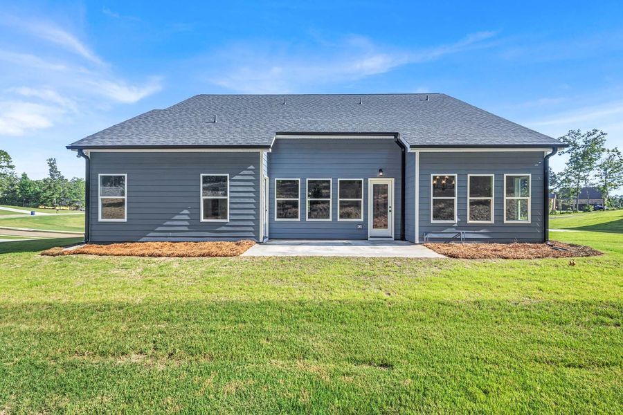 Back of a blue house with many windows, patio, and green lawn under blue sky.