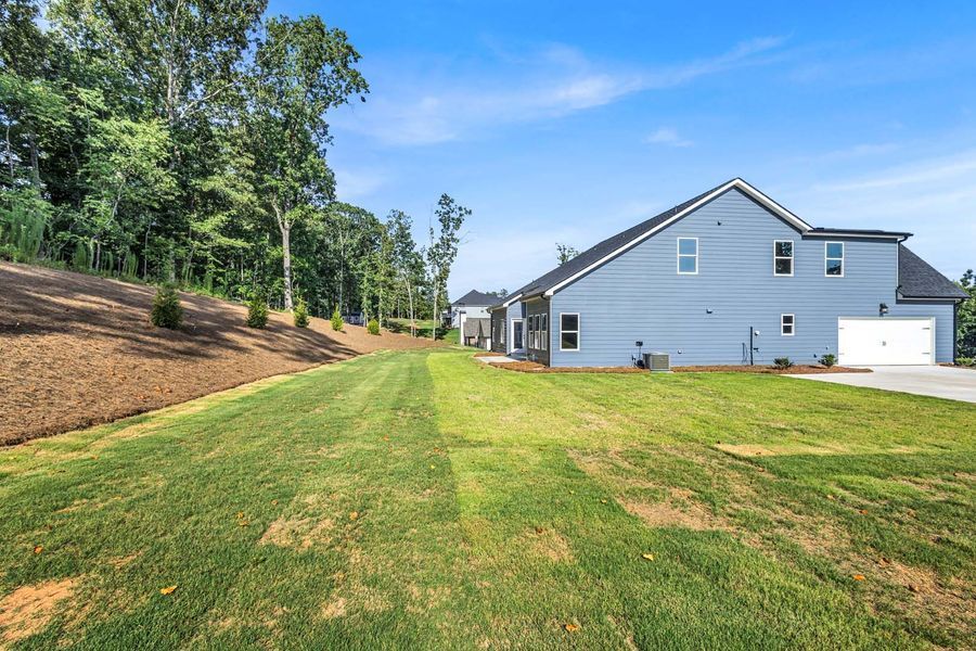 Side view of a light gray house with a manicured lawn and trees under a blue sky.