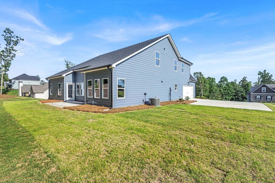 Back of a blue house with a patio on a grassy lot, under a blue sky.