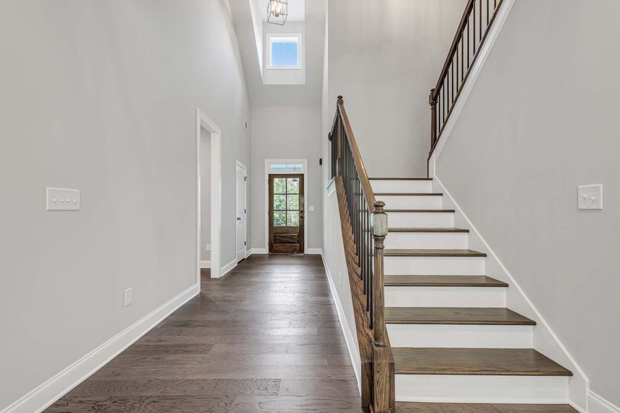 Entryway with wood floors, staircase, and front door. Gray walls, dark wood door and banister.
