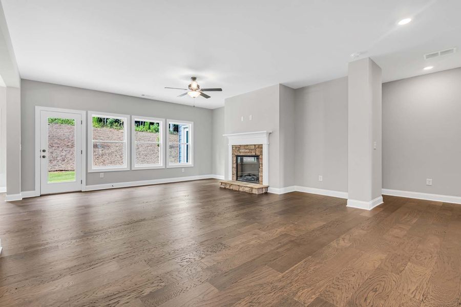 Empty living room with dark wood floors, fireplace, and large windows.