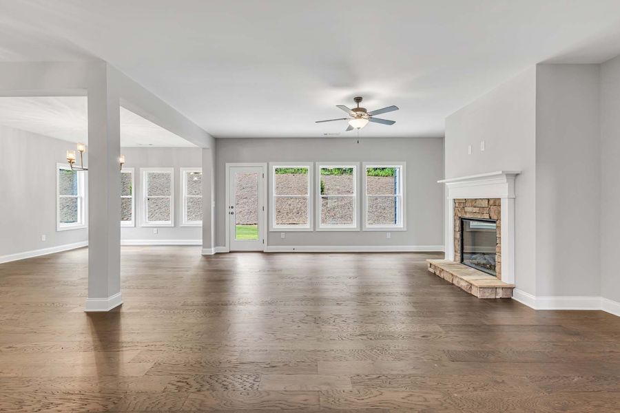 Empty living room with hardwood floors, fireplace, windows, and light gray walls.