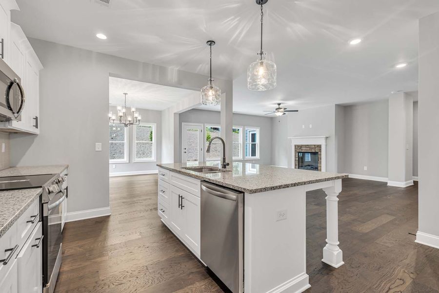 Open-concept kitchen with a white island and granite countertop, connected to a living area with a fireplace.