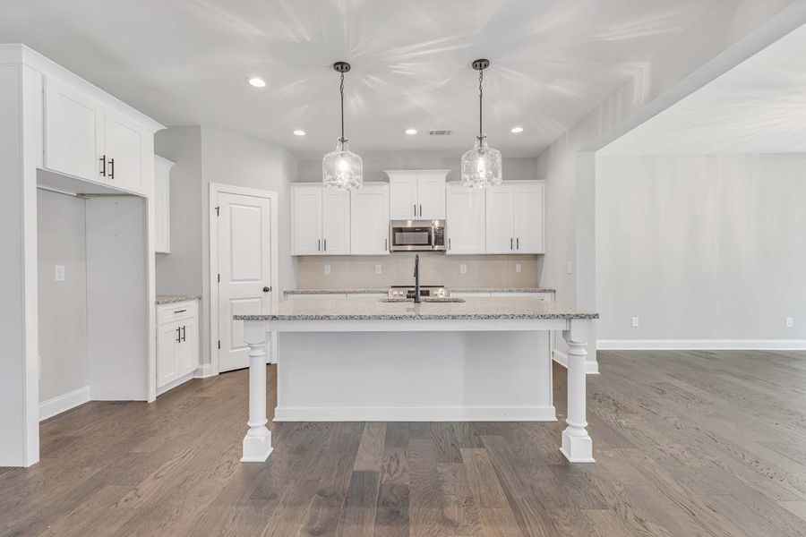 White kitchen with island, light-colored cabinets, dark wood floors, and two pendant lights.