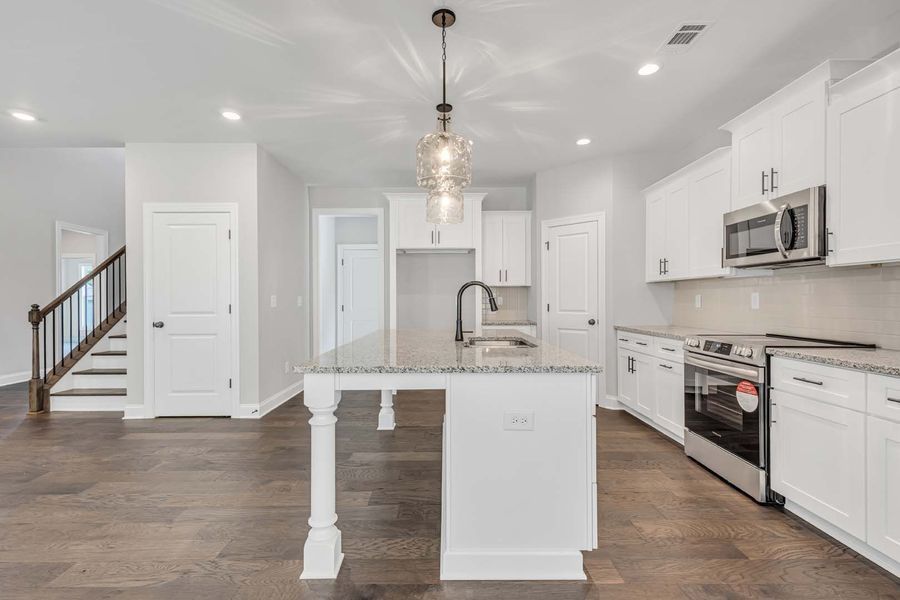 Bright white kitchen with island, stainless appliances, and dark wood floors.