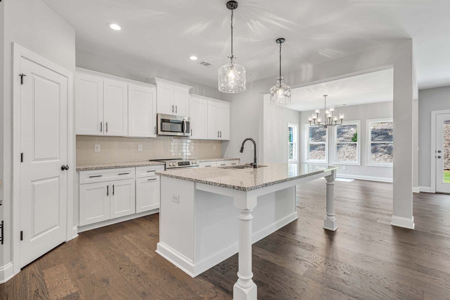 White kitchen with island, granite countertop, dark wood floors, and view into living area.