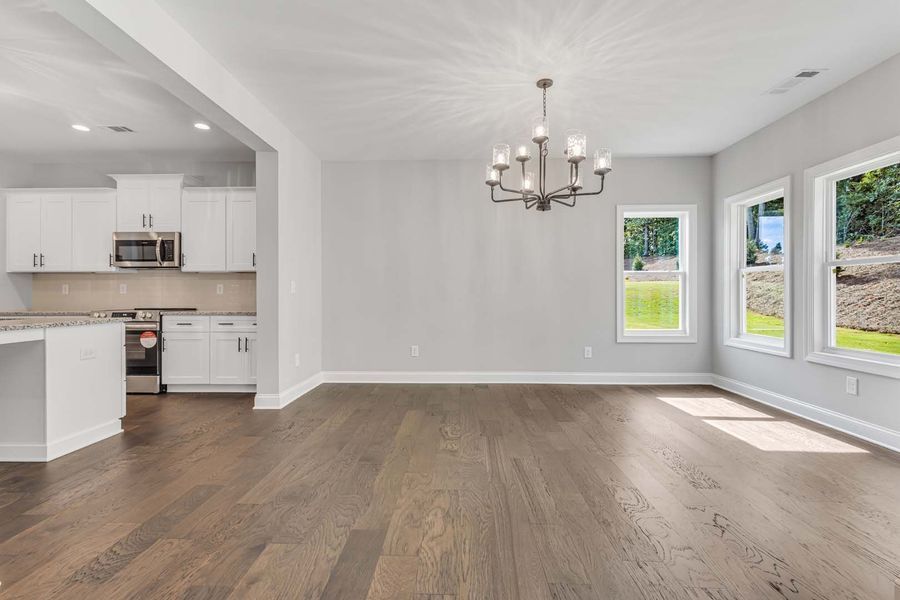 Empty dining room with hardwood floors, gray walls, white trim, and a chandelier.
