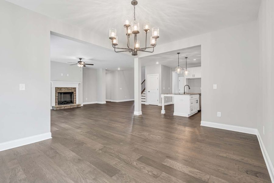 An open floor plan with gray walls, hardwood floors, and a chandelier. Includes a living room, kitchen, and fireplace.