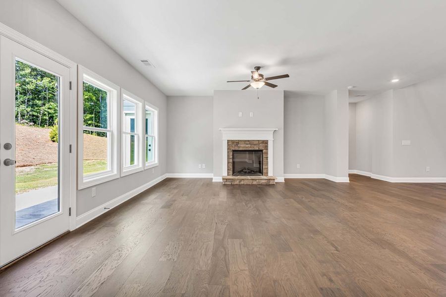 Empty living room with fireplace, windows, and hardwood floors.