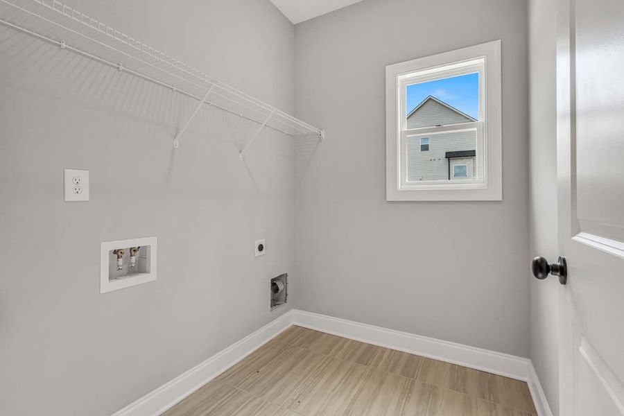 Empty laundry room with washer/dryer hookups, a window, wire shelving, and light gray walls.