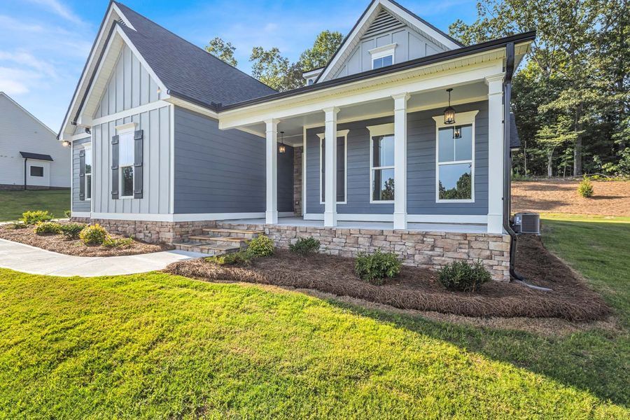 Blue house with white columns and stone base, porch, and green lawn.