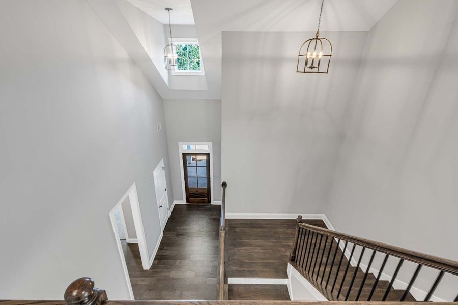 High-angle view of a foyer with dark wood floors, stairs with a wooden railing, and a front door.