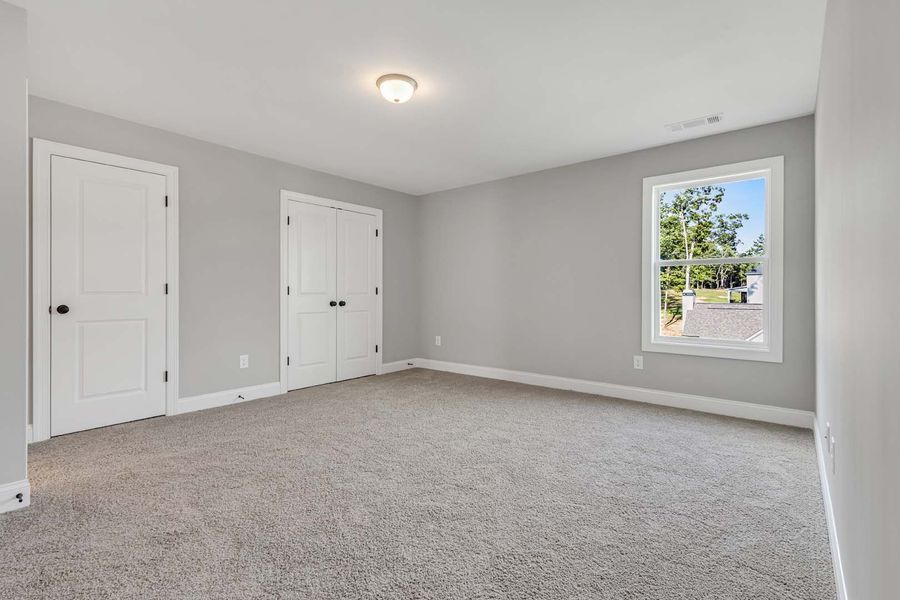 Empty gray bedroom with white doors, window, and carpet.