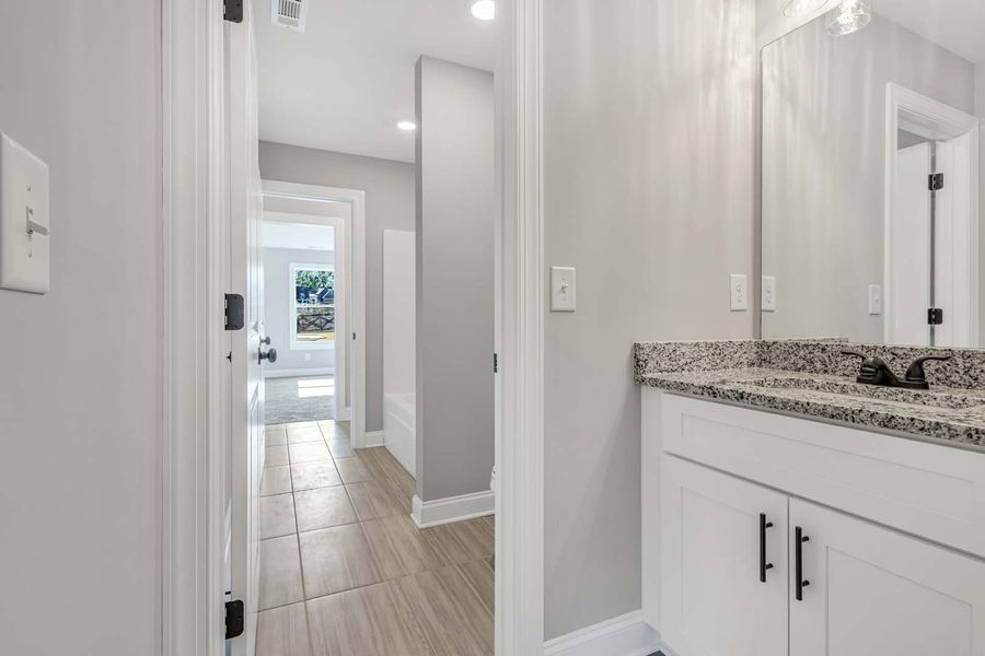 Bathroom hallway with white cabinetry, granite countertop, and a view into a bathroom.