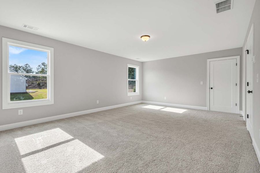 Empty bedroom with gray walls, carpet, and two windows letting in sunlight.