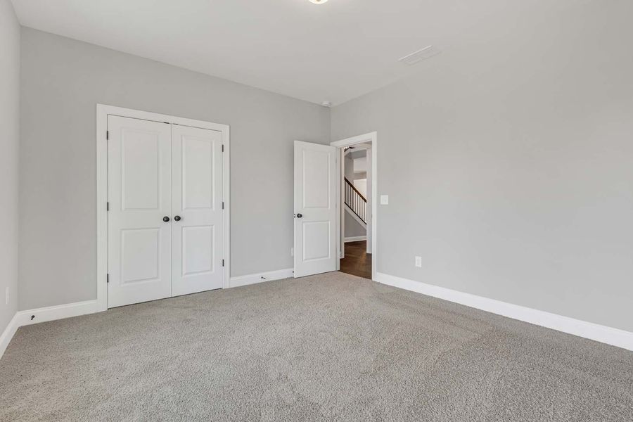 Empty bedroom with gray carpet, light gray walls, white trim, and two white doors.