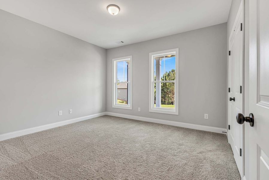 Empty bedroom with gray walls, carpet, two windows, and a white door.