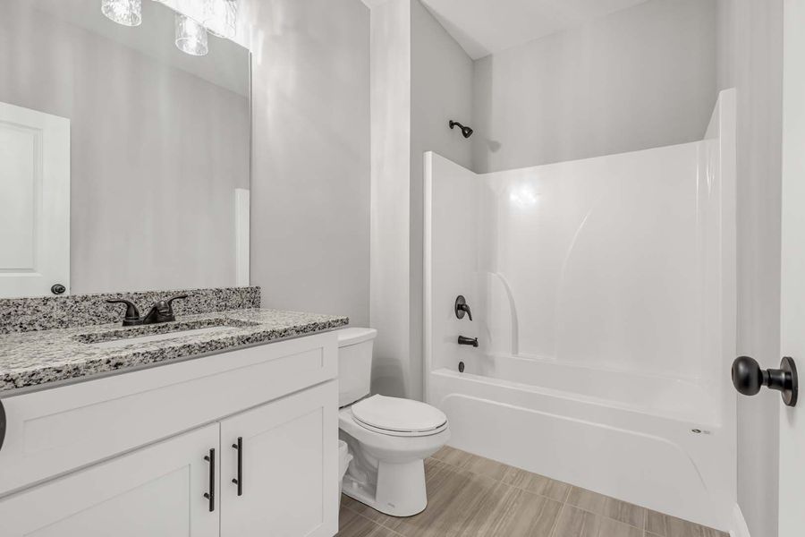 White bathroom with a tub/shower combo, white toilet, and a granite countertop.