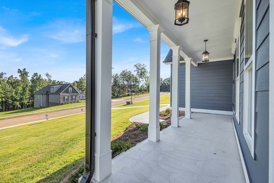 A porch with white columns and black light fixtures. View of a green yard and houses in the distance.