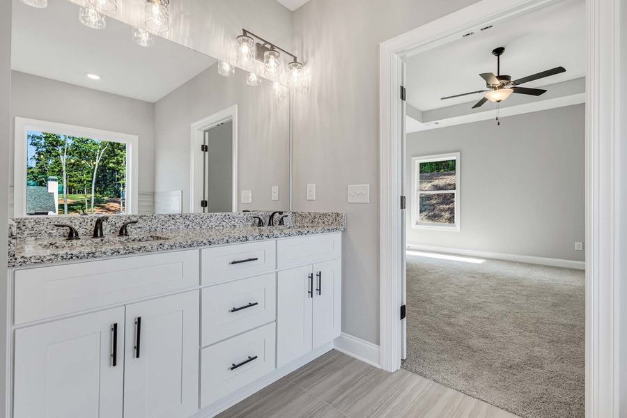 Bathroom with white vanity, granite countertop, and open doorway to a bedroom with a ceiling fan.