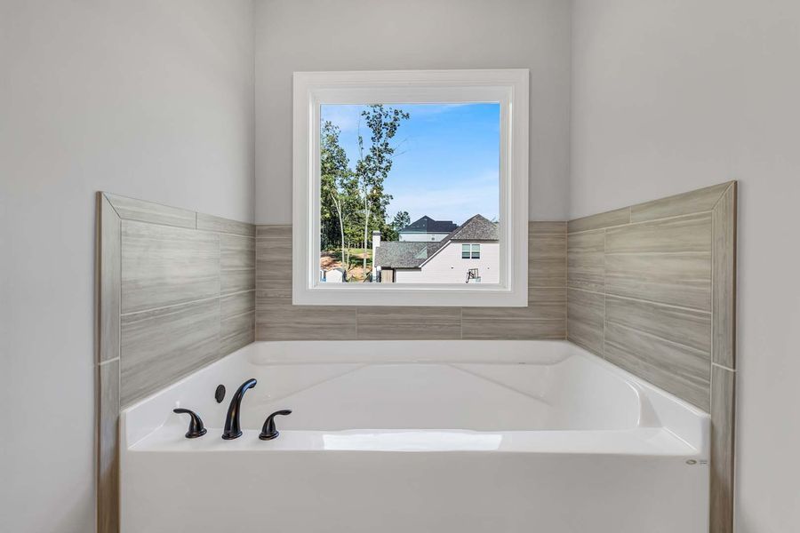 A built-in white bathtub with black fixtures beneath a window in a bathroom, with gray tile accents.
