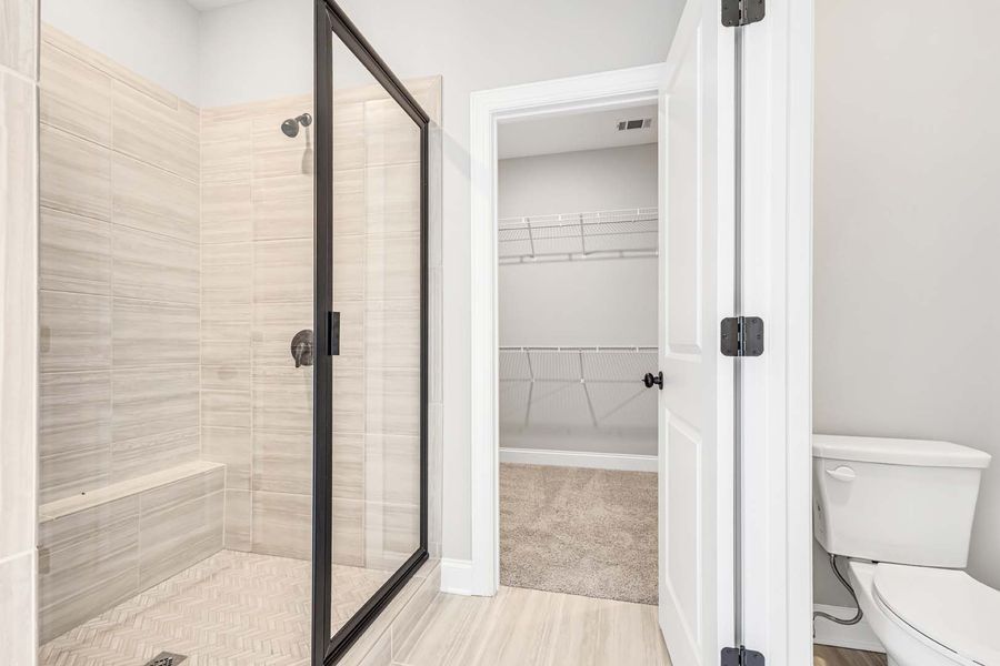 Bathroom with a glass shower, white toilet, and open door to a closet.
