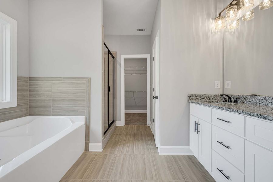 Modern bathroom with white vanity, bathtub, and a walk-in closet. Light gray walls and tile floor.