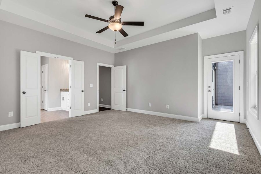 Spacious bedroom with gray walls, carpet, and white trim, with doors leading to the bathroom and outside.