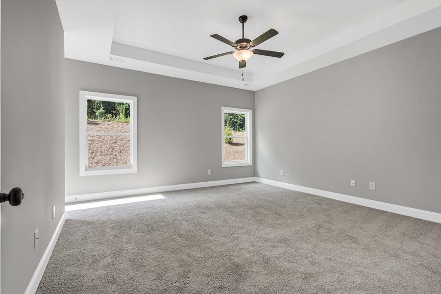 Empty bedroom with gray walls and carpet; two windows; ceiling fan.