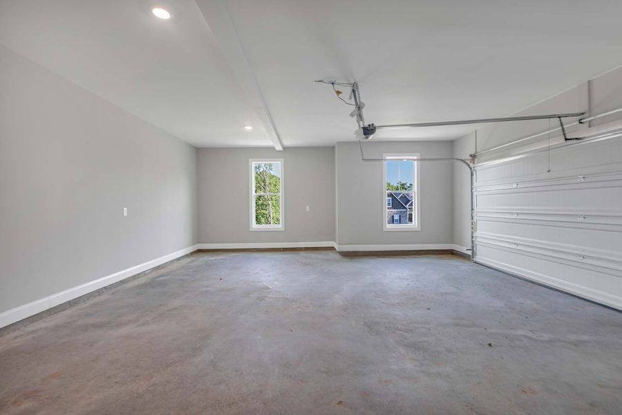 Empty, freshly painted two-car garage with gray walls, concrete floor, and a white garage door.