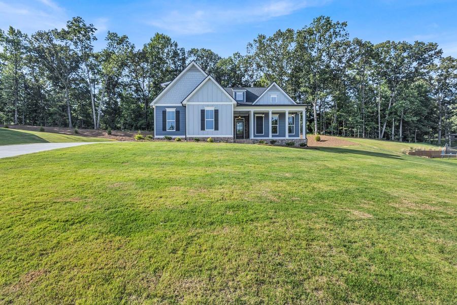 Blue-gray house with black shutters, porch, and green lawn. Trees in background, blue sky.