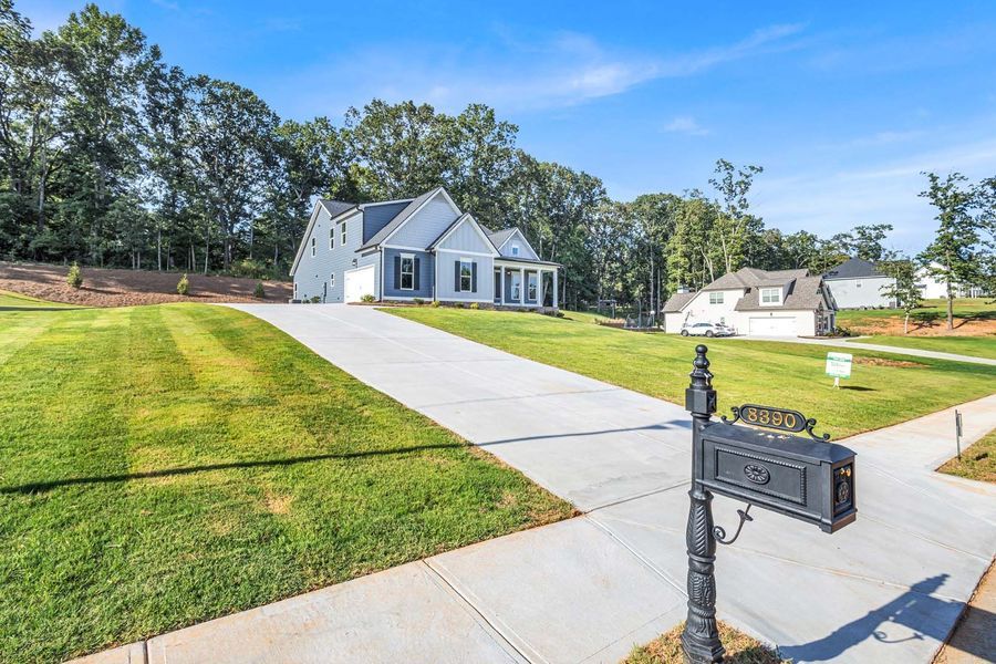 Gray house with white trim, a long concrete driveway, and a black mailbox on a sunny day.