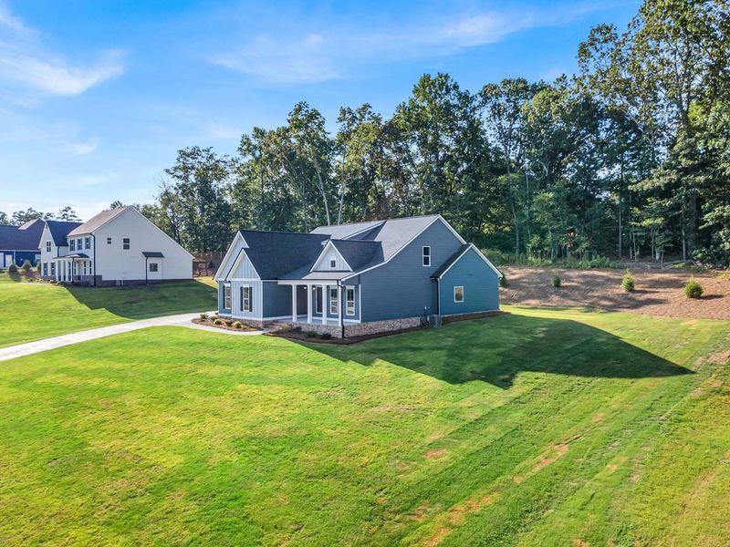 Blue house with white trim, on a grassy hill with trees in the background.