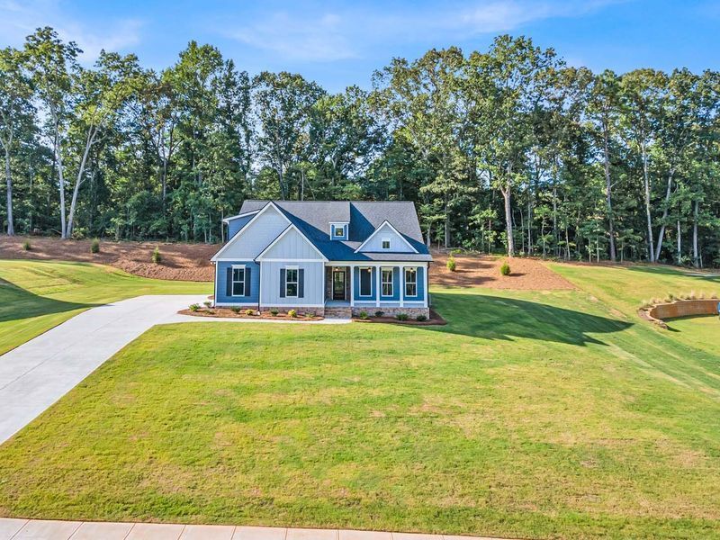 Blue house with black shutters on a grassy lot, driveway leading to the front door, trees in the background.