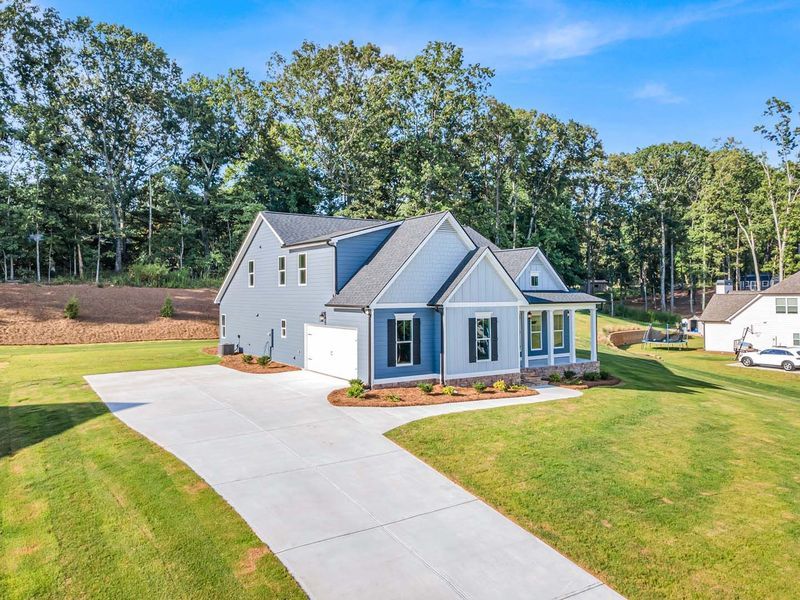 Blue and grey house with a long driveway, surrounded by grass and trees on a sunny day.
