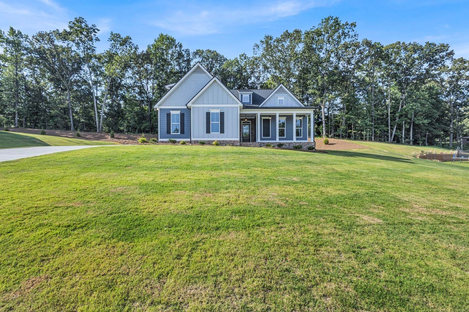 Blue and gray house with a porch, set on a grassy hill with trees in the background.
