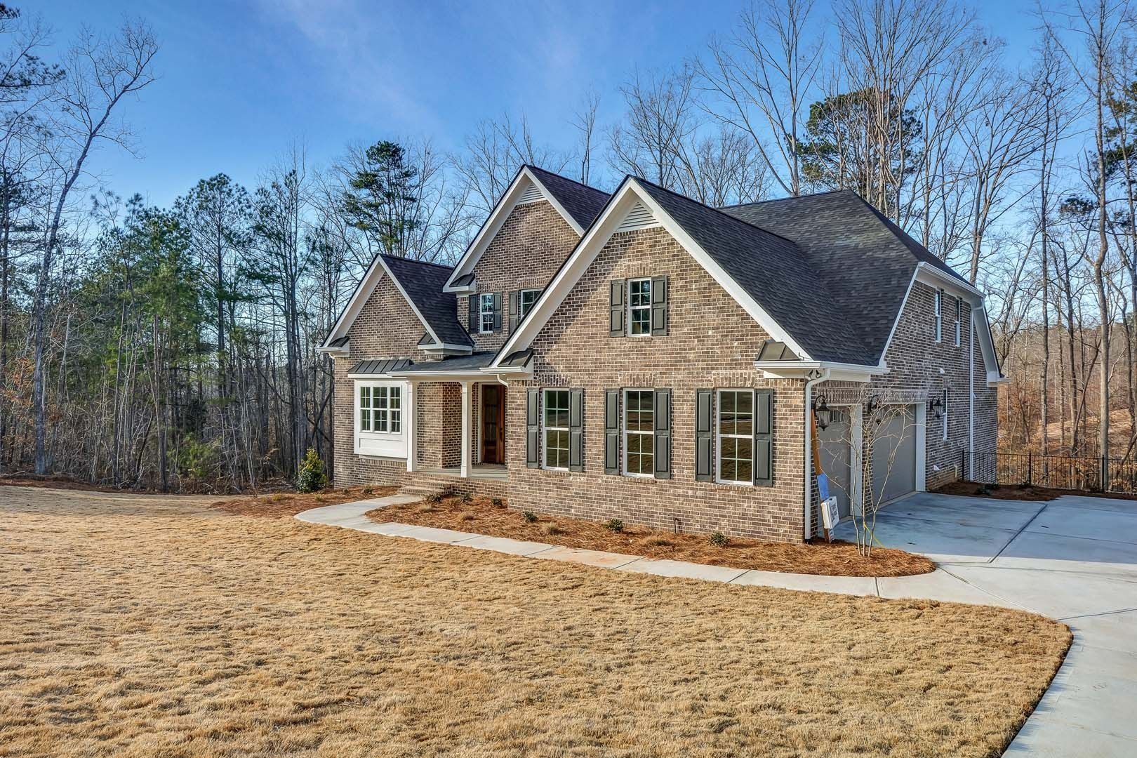 Two-story brick house with brown roof and driveway on a lawn surrounded by trees.